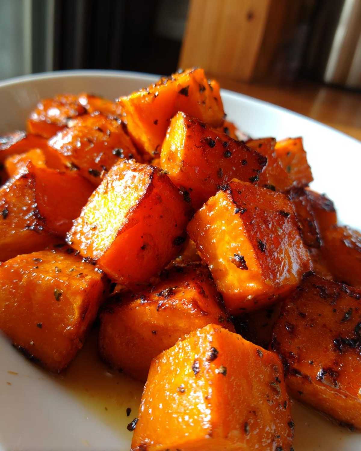 Close-up of glossy, cubed roasted sweet potatoes seasoned with dark spices, ready to serve.
