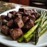 Close-up of juicy steak bites coated in garlic butter next to bright green asparagus spears from Sheet Pan Garlic Butter Steak and Asparagus.