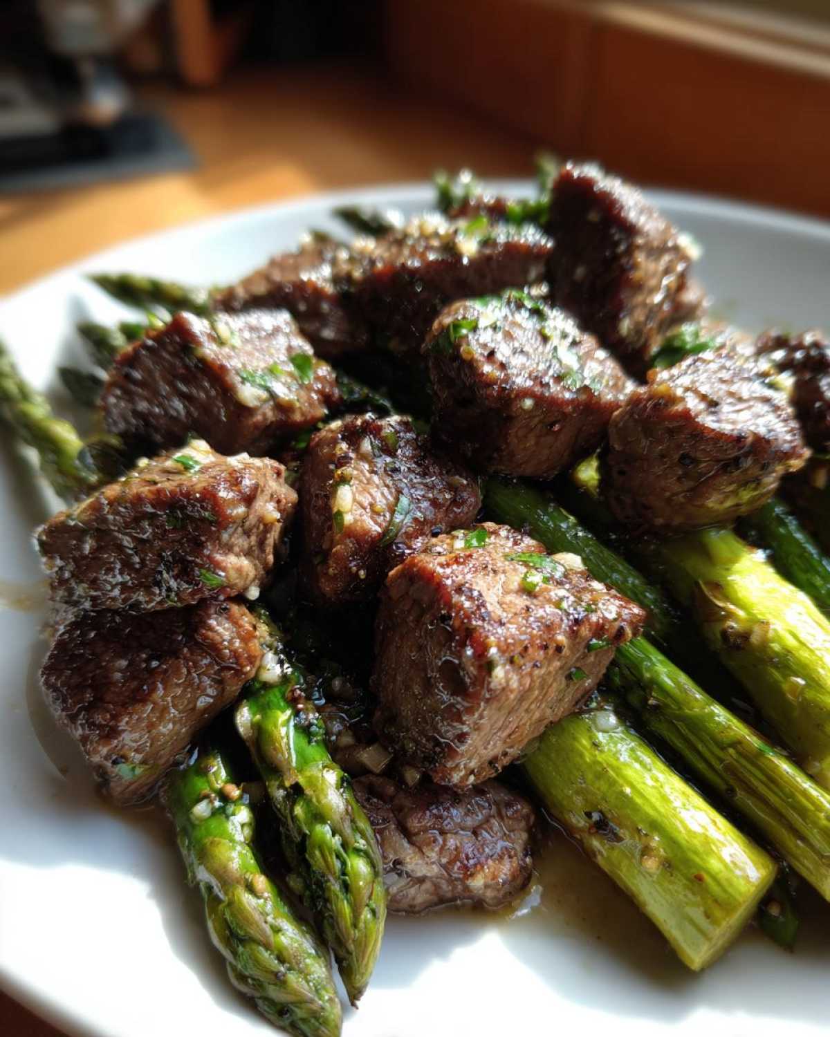 Close-up of juicy steak bites served over bright green asparagus, coated in garlic butter sauce.