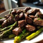 Close-up of juicy steak bites served over roasted asparagus, featuring Sheet Pan Garlic Butter Steak and Asparagus.
