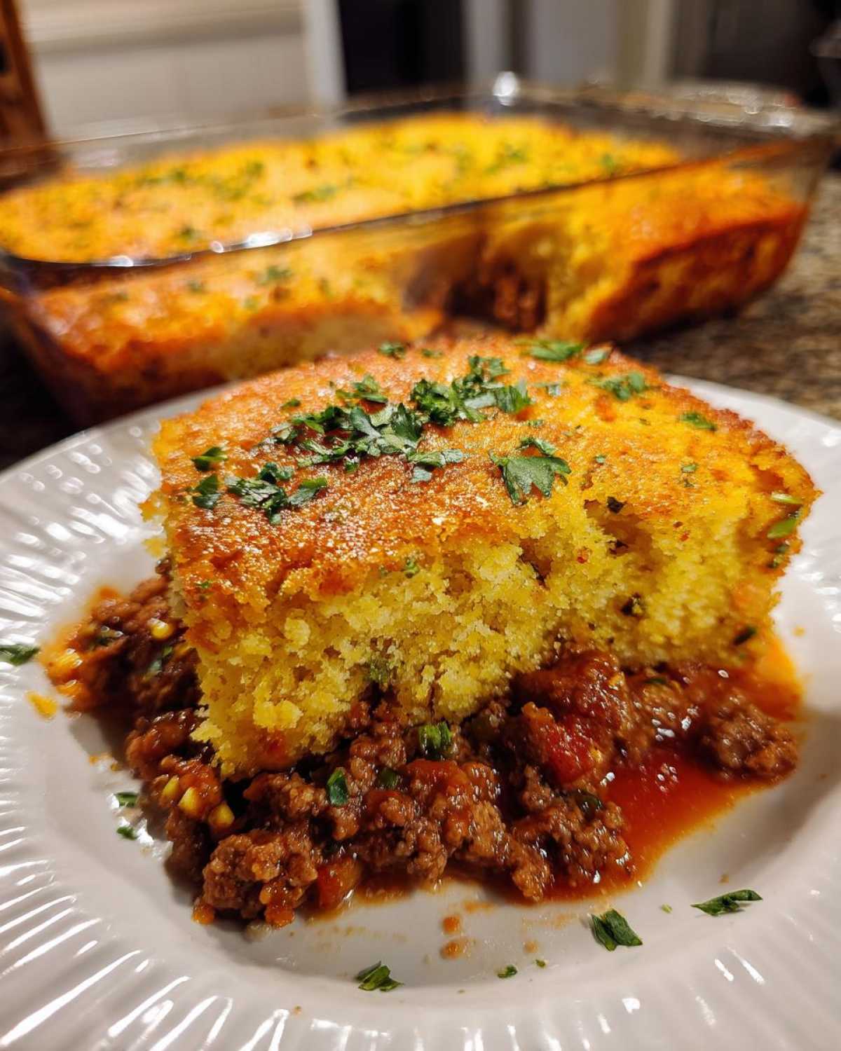 A serving of sloppy joe cornbread casserole featuring a square of golden cornbread over savory meat sauce, garnished with parsley.