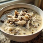 A close-up of a white bowl filled with rich Slow Cooker Creamy Chicken and Wild Rice Soup, topped with shredded chicken.