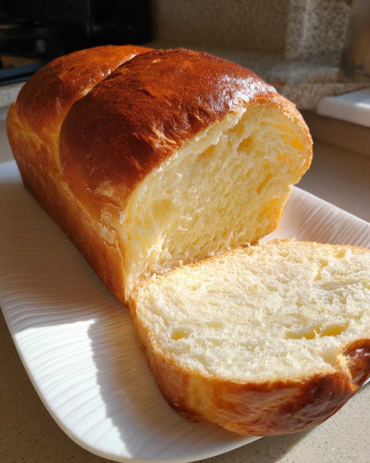 A loaf of soft condensed milk bread, partially sliced, showing its fluffy interior and golden-brown crust.