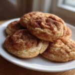 A stack of soft, freshly baked snickerdoodles coated in cinnamon sugar on a white plate.