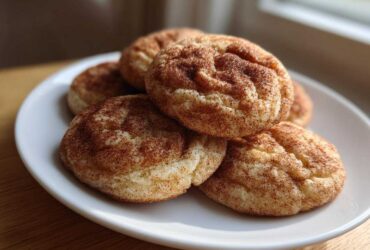 A stack of soft, freshly baked snickerdoodles coated in cinnamon sugar on a white plate.