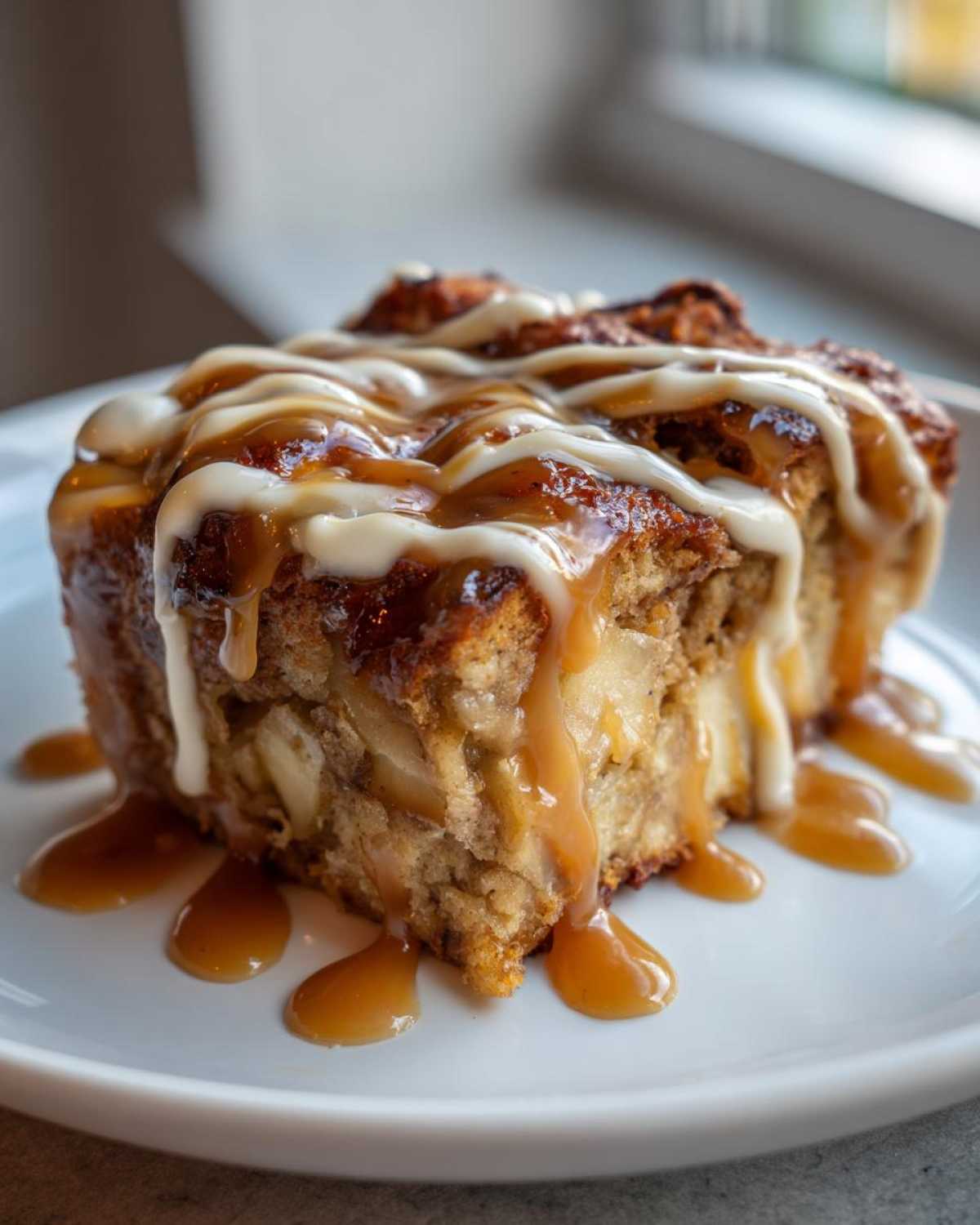 Close-up of a serving of ultimate apple bread pudding topped with caramel and vanilla icing.