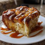 A square slice of warm apple bread pudding topped with caramel and white icing drizzle.