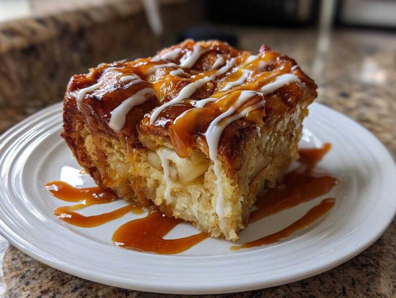 A square slice of warm apple bread pudding topped with caramel and white icing drizzle.