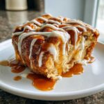 A close-up of a warm slice of apple bread pudding topped with caramel and vanilla icing.