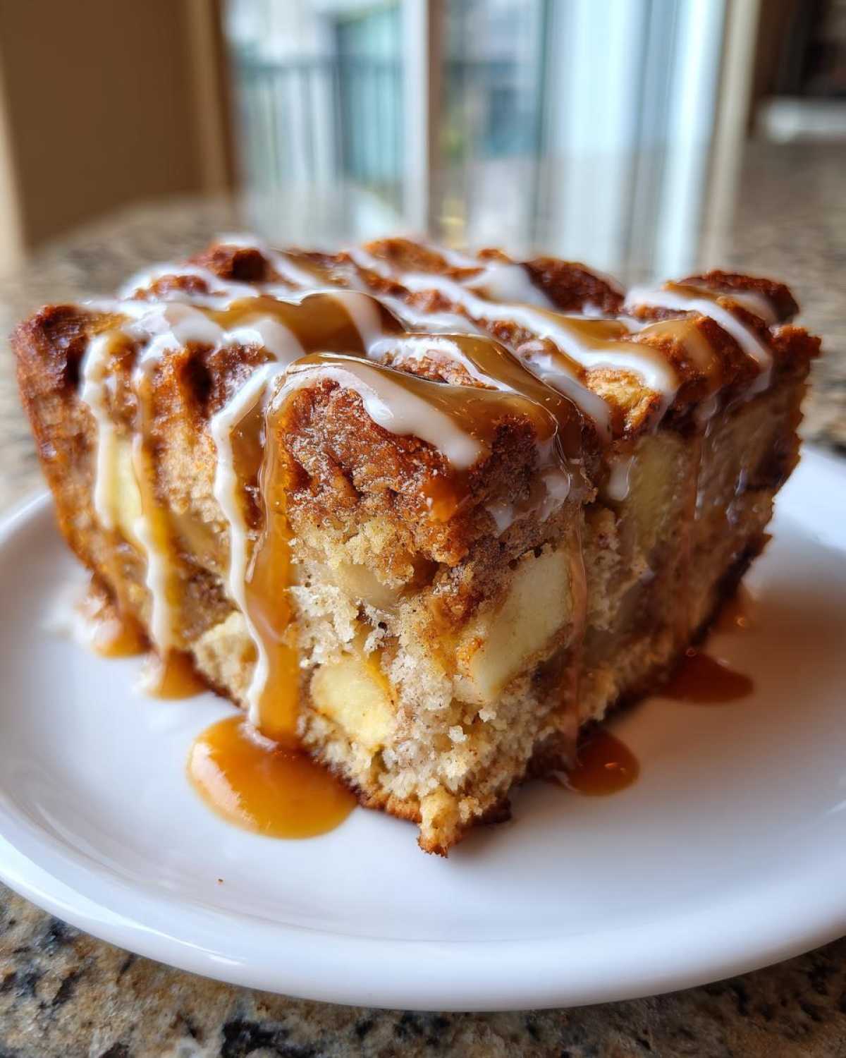 A close-up of a moist slice of apple bread pudding topped with caramel and white icing drizzle.