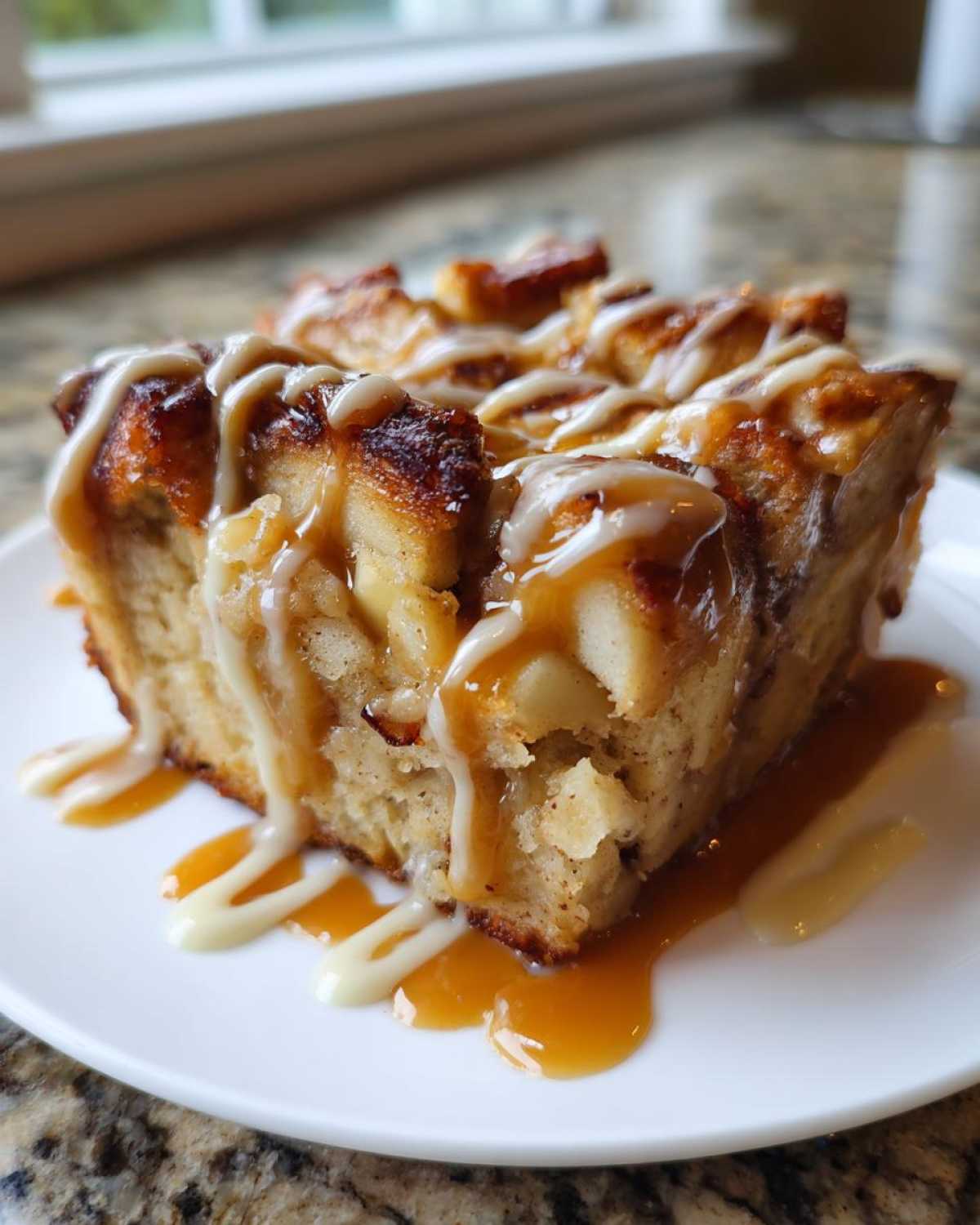 Close-up of a square slice of ultimate apple bread pudding drizzled with caramel and vanilla glaze.