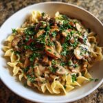 A close-up of creamy Vegan Mushroom Stroganoff served over wide egg noodles and garnished with fresh parsley.
