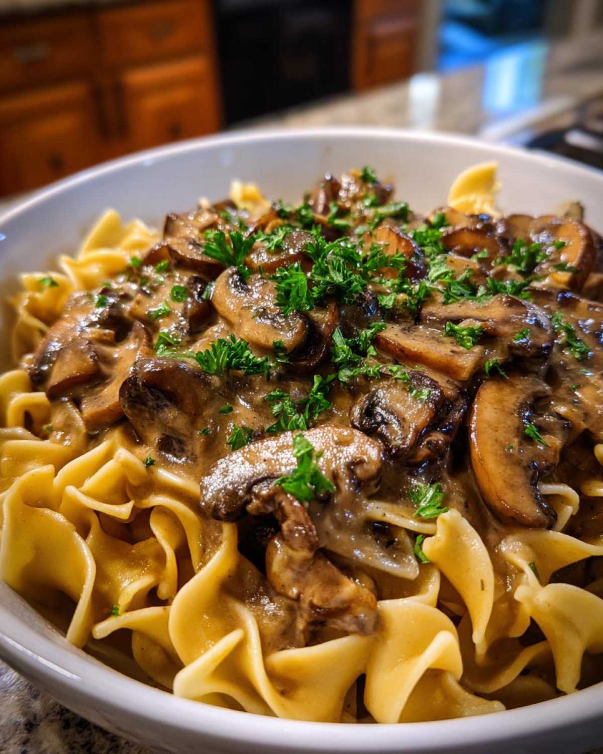 A close-up of rich Vegan Mushroom Stroganoff served over wide egg noodles, garnished with fresh parsley.