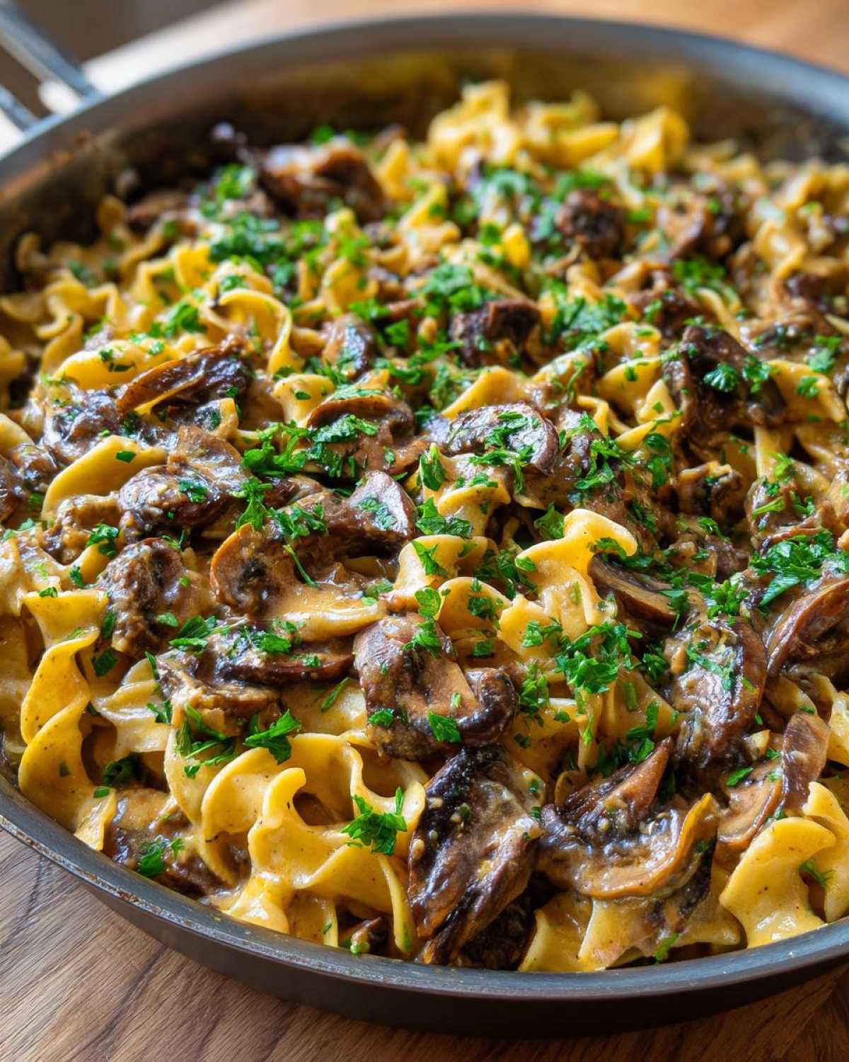 Close-up of creamy Vegan Mushroom Stroganoff with wide egg noodles and fresh parsley garnish.