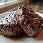 Two thick, grilled portobello mushrooms seasoned with herbs, resembling steak, coated in a balsamic glaze.