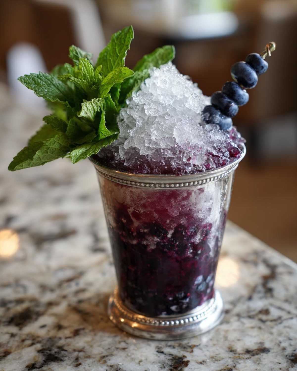 A vibrant Blueberry Mint Julep Cocktail served in a silver cup, topped with crushed ice, fresh mint, and a blueberry skewer.