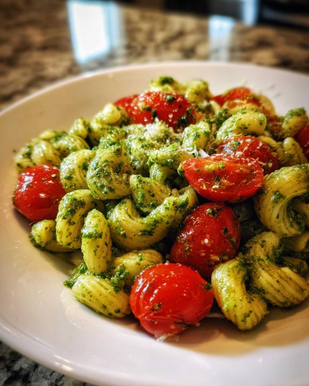 A close-up of Broccoli Pesto Pasta Salad featuring corkscrew pasta coated in green pesto, mixed with bright red cherry tomatoes.