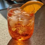 Close-up of a refreshing, bubbly Aperol Spritz Cocktail filled with ice and garnished with an orange slice.