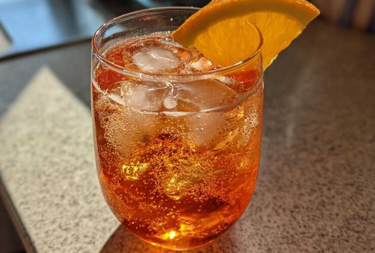 Close-up of a refreshing, bubbly Aperol Spritz Cocktail filled with ice and garnished with an orange slice.