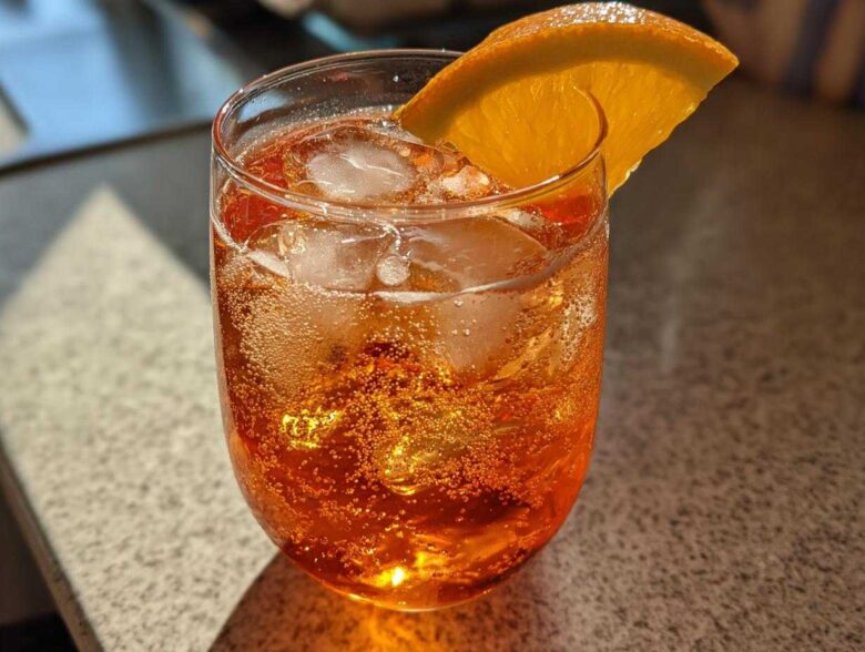 Close-up of a refreshing, bubbly Aperol Spritz Cocktail filled with ice and garnished with an orange slice.