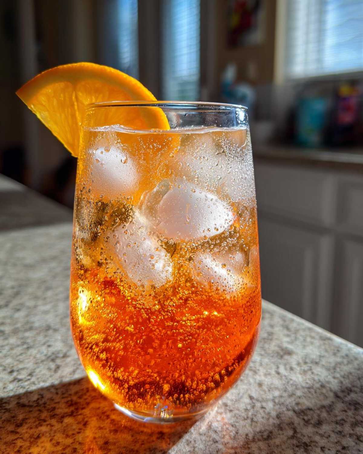 Close-up of a tall glass filled with a Bubbly Aperol Spritz Cocktail, ice, and an orange slice garnish.