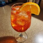 A close-up of a chilled Bubbly Aperol Spritz Cocktail filled with ice and garnished with a bright orange slice.