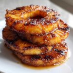 A stack of three glistening Caramelized Grilled Pineapple Rings sitting in sweet syrup on a white plate.