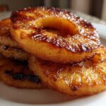 Close-up of a stack of glistening Caramelized Grilled Pineapple Rings on a white plate.