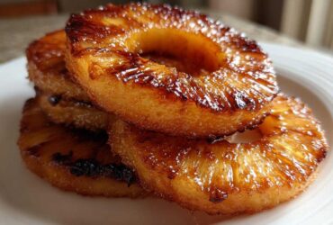 Close-up of a stack of glistening Caramelized Grilled Pineapple Rings on a white plate.