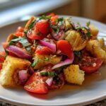 A close-up of a serving of Classic Panzanella Salad featuring tomatoes, red onion, basil, and toasted bread cubes.