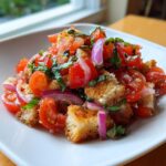A close-up of a serving of Classic Panzanella Salad featuring juicy tomatoes, toasted bread chunks, red onion, and fresh basil.