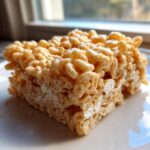 A single, perfectly cut square of Classic Rice Krispie Treats Squares resting on a white plate.