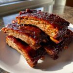 A stack of tender, saucy Classic Slow Cooker BBQ Ribs glistening with rich BBQ sauce on a white plate.