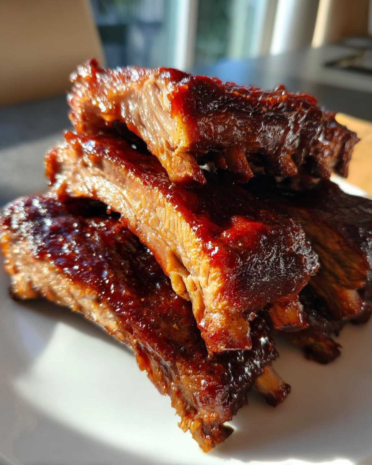 A stack of tender, glazed Classic Slow Cooker BBQ Ribs glistening under natural light on a white plate.