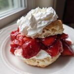 A close-up of a Classic Strawberry Shortcake with Whipped Cream, featuring a biscuit split and filled with macerated strawberries and topped with a dollop of cream.