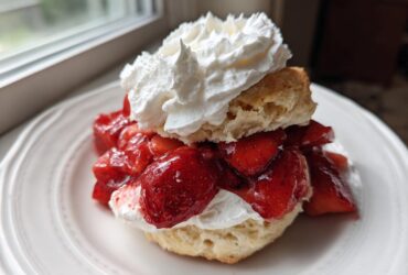 A close-up of a Classic Strawberry Shortcake with Whipped Cream, featuring a biscuit split and filled with macerated strawberries and topped with a dollop of cream.