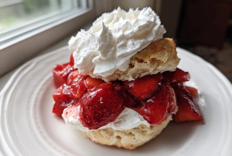 A close-up of a Classic Strawberry Shortcake with Whipped Cream, featuring a biscuit split and filled with macerated strawberries and topped with a dollop of cream.
