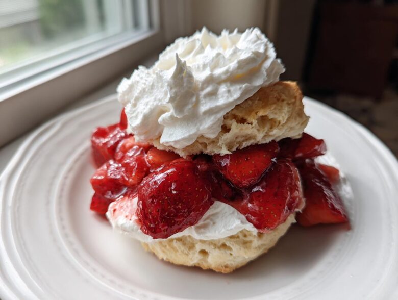 A close-up of a Classic Strawberry Shortcake with Whipped Cream, featuring a biscuit split and filled with macerated strawberries and topped with a dollop of cream.