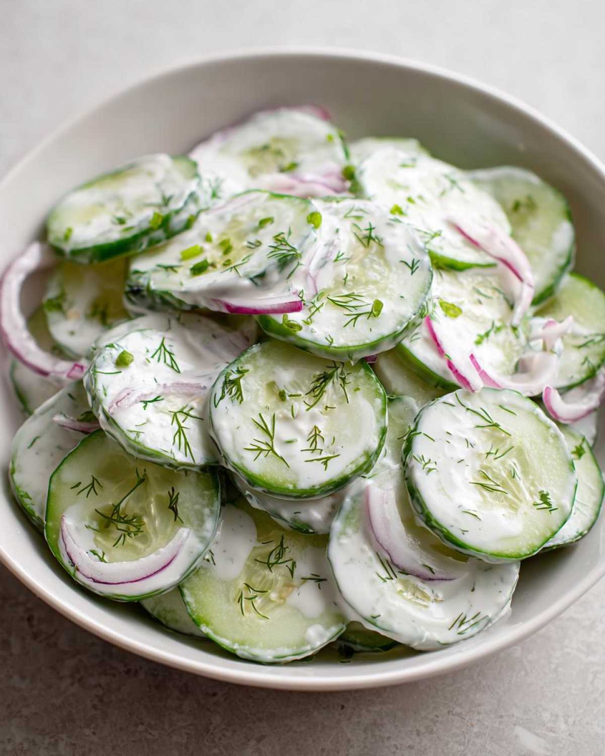 Close-up view of a bowl filled with slices of Creamy Dill Cucumber Salad, tossed in a white dressing and topped with fresh dill.