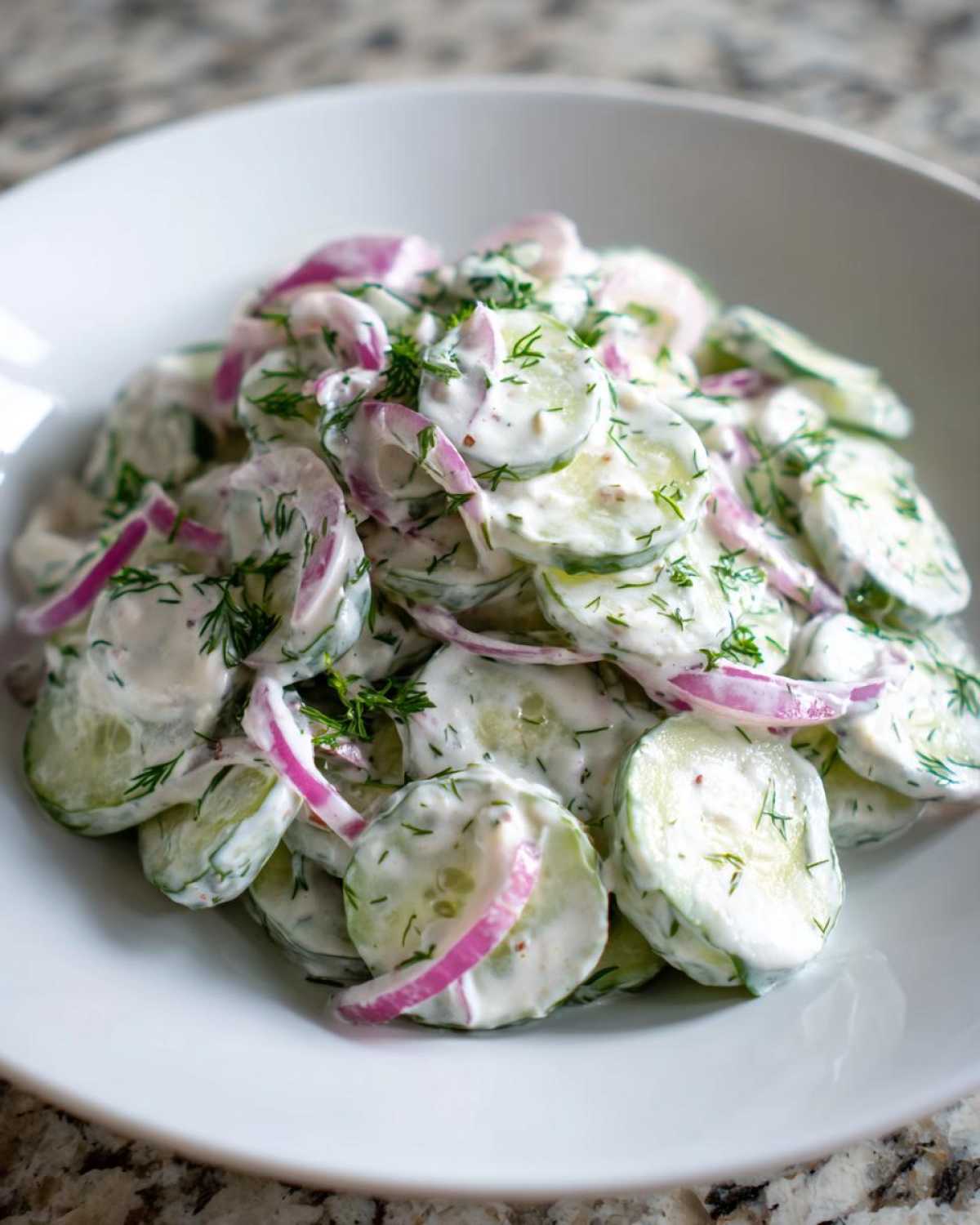 Close-up of sliced cucumbers coated in a creamy white dressing with red onion slices and fresh dill, showcasing the Creamy Dill Cucumber Salad.