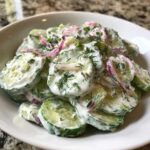 A close-up of sliced cucumbers coated in a creamy dressing with fresh dill and red onion, showcasing the Creamy Dill Cucumber Salad.