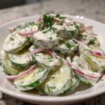 A close-up of sliced cucumbers coated in a creamy dressing with fresh dill and red onion, showcasing the Creamy Dill Cucumber Salad.