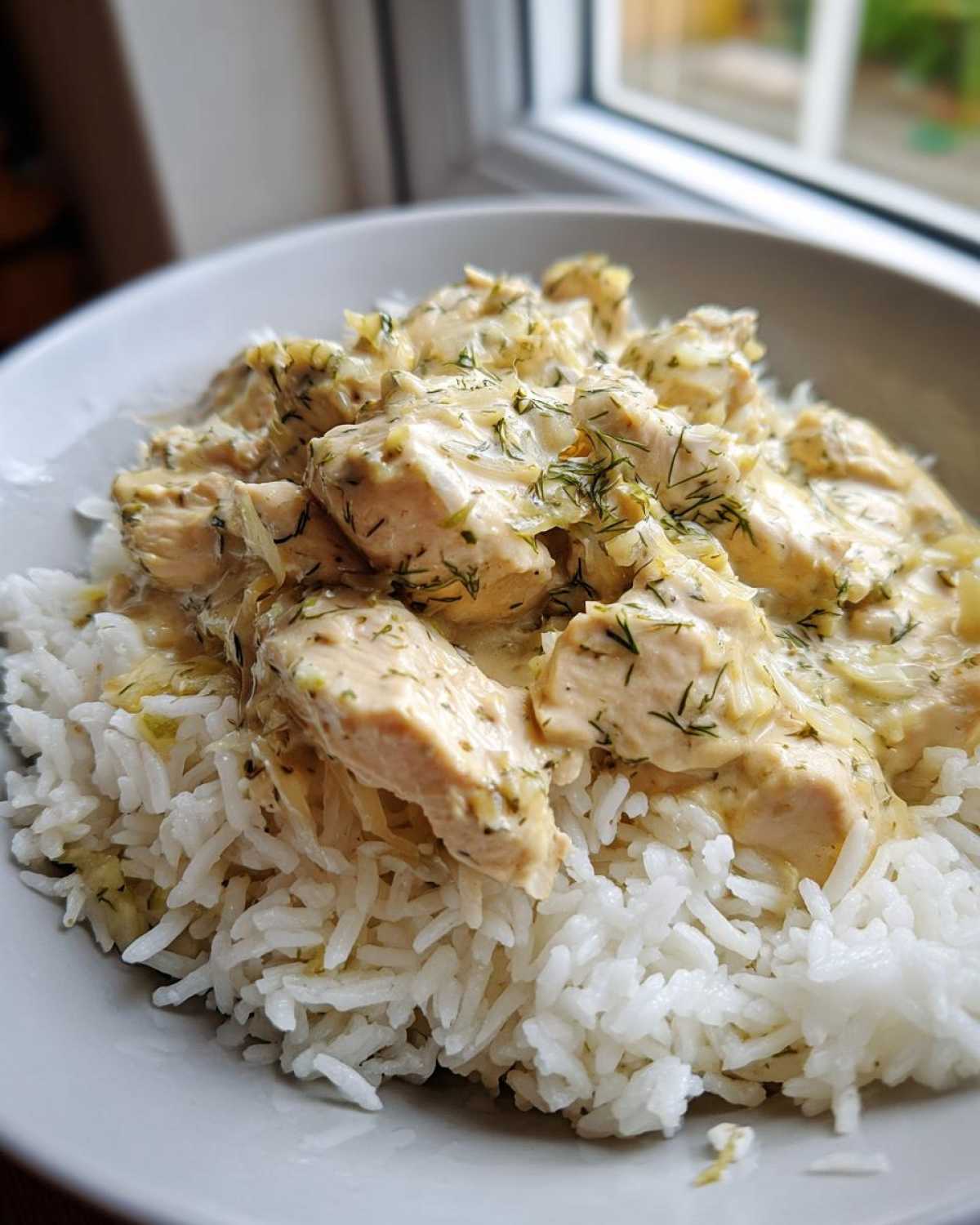 Close-up of tender chicken pieces in a creamy sauce with dill served over white rice, featuring the Dump-and-Bake Chicken Tzatziki Recipe.