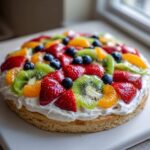 A vibrant Easy Fruit Pizza with Sugar Cookie Crust topped with strawberries, kiwi, blueberries, and mandarin oranges over cream.