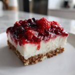 Close-up of a single serving of Easy No-Bake Cheesecake Bars featuring a thick graham cracker crust, creamy white filling, and vibrant mixed berry topping.