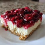 A close-up of one square slice of Easy No-Bake Cheesecake Bars with a thick layer of bright red berry topping.
