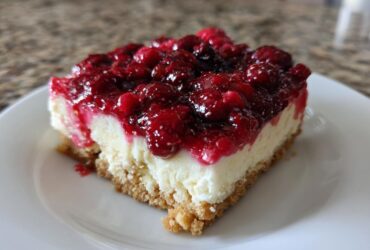 A close-up of one square slice of Easy No-Bake Cheesecake Bars with a thick layer of bright red berry topping.