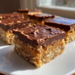 A close-up of a square of Easy No-Bake Peanut Butter Chocolate Bars showing the crunchy base, creamy peanut butter layer, and chocolate topping.