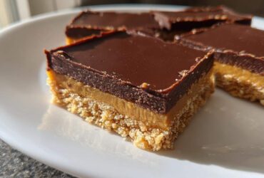 A close-up of a square Easy No-Bake Peanut Butter Chocolate Bars showing three distinct layers: crust, peanut butter filling, and chocolate topping.