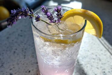 Close-up of a tall glass filled with ice and Fragrant Lavender Lemonade, garnished with fresh lavender sprigs and a lemon slice.